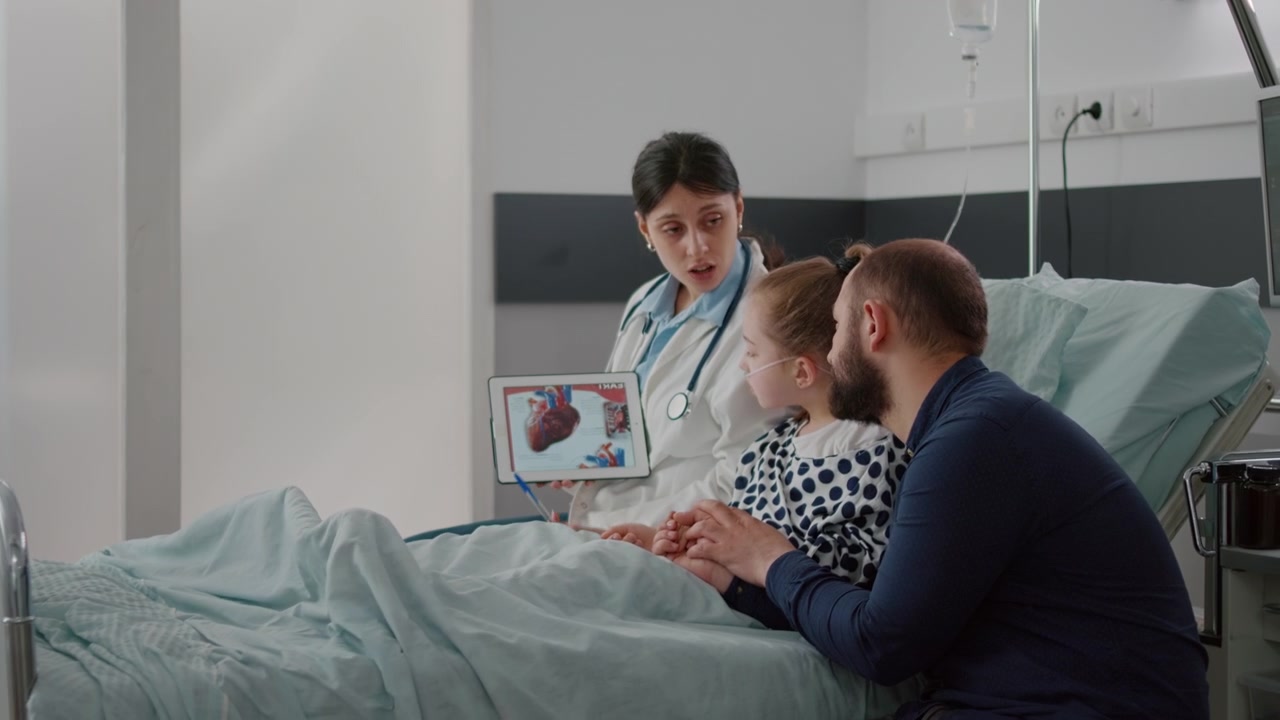 Médico explicando la anatomía del corazón a un paciente joven y a su padre en una habitación de hospital