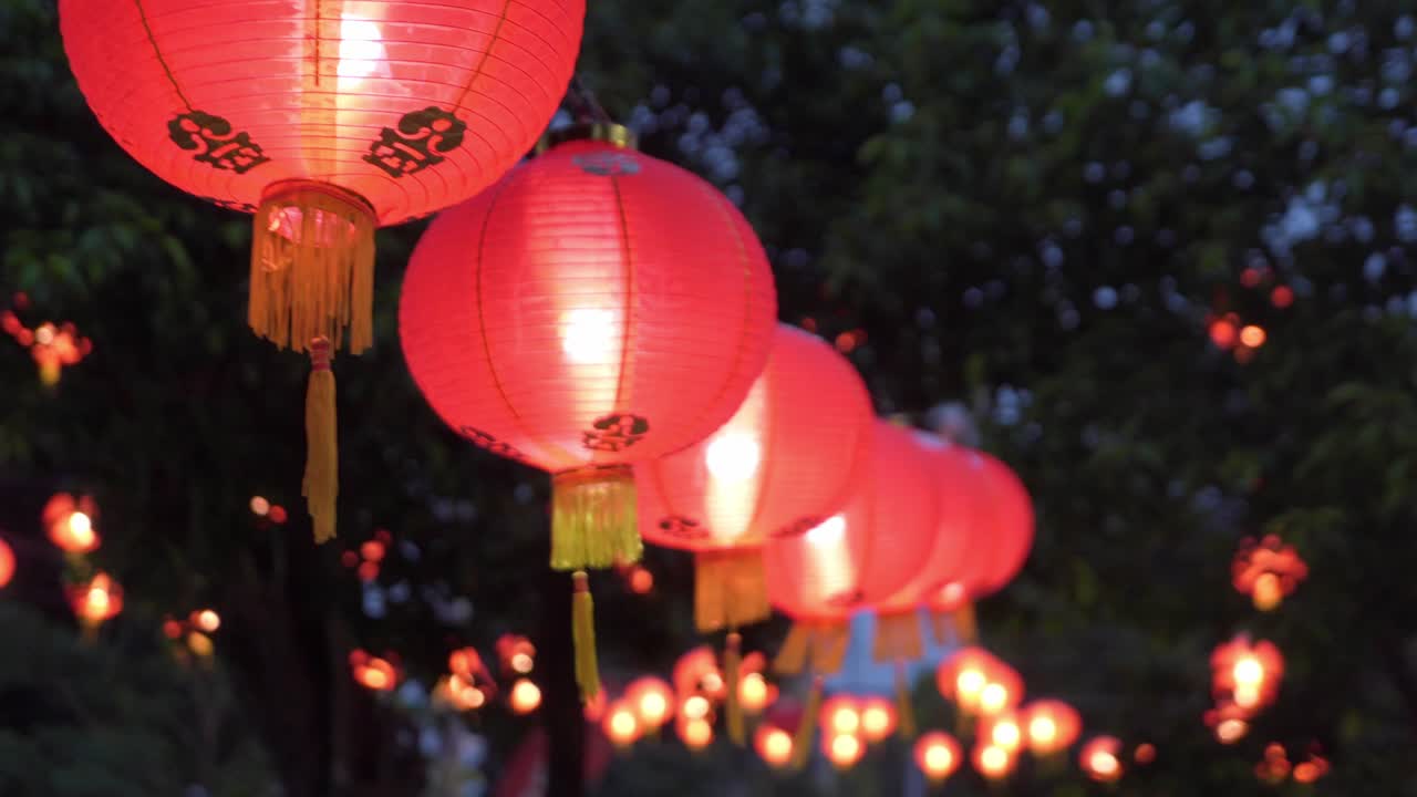 Red Chinese lanterns glowing at dusk during festival, hanging outdoors with trees in background