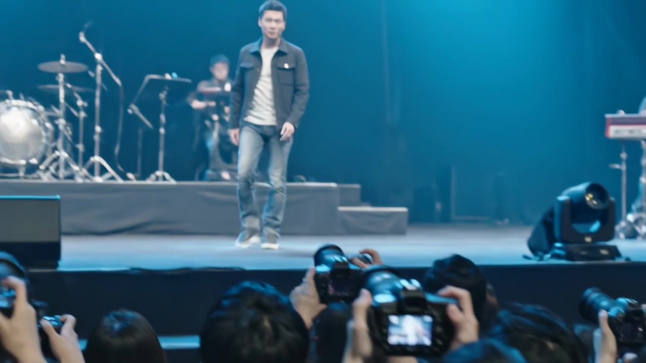 高舉雙手的亞洲音樂家，粉絲在舞台附近舉起單反相機，穿著深色外套，走上舞台