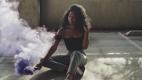 beautiful young woman modeling with purple smoke grenade in dramatic moody lighting