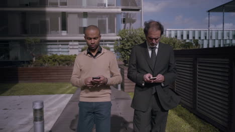 Concentrated-businessmen-walking-and-using-smartphones-near-office-buildings