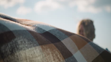 a woman with her face slightly blurred and hair covering her face holds a plaid scarf as the wind gently blows it. the scene captures a serene moment of connection with nature