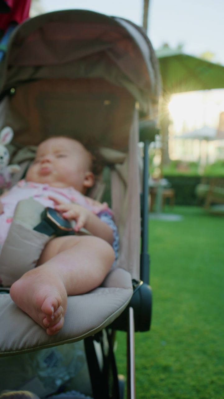 Vertical close-up of a baby lying in a stroller on a lawn, focus on the baby's foot