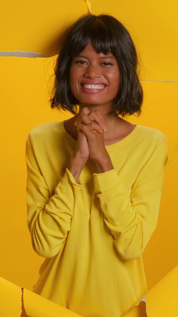 Donna asiatica felicissima che ride e applaude su uno sfondo di carta gialla strappata