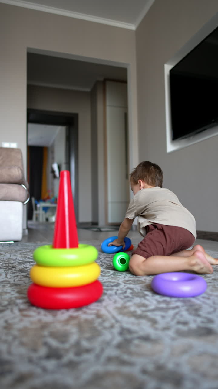 Cute baby boy sits on the floor building a pyramid. Active toddler boy playing at home with toys. Vertical video.