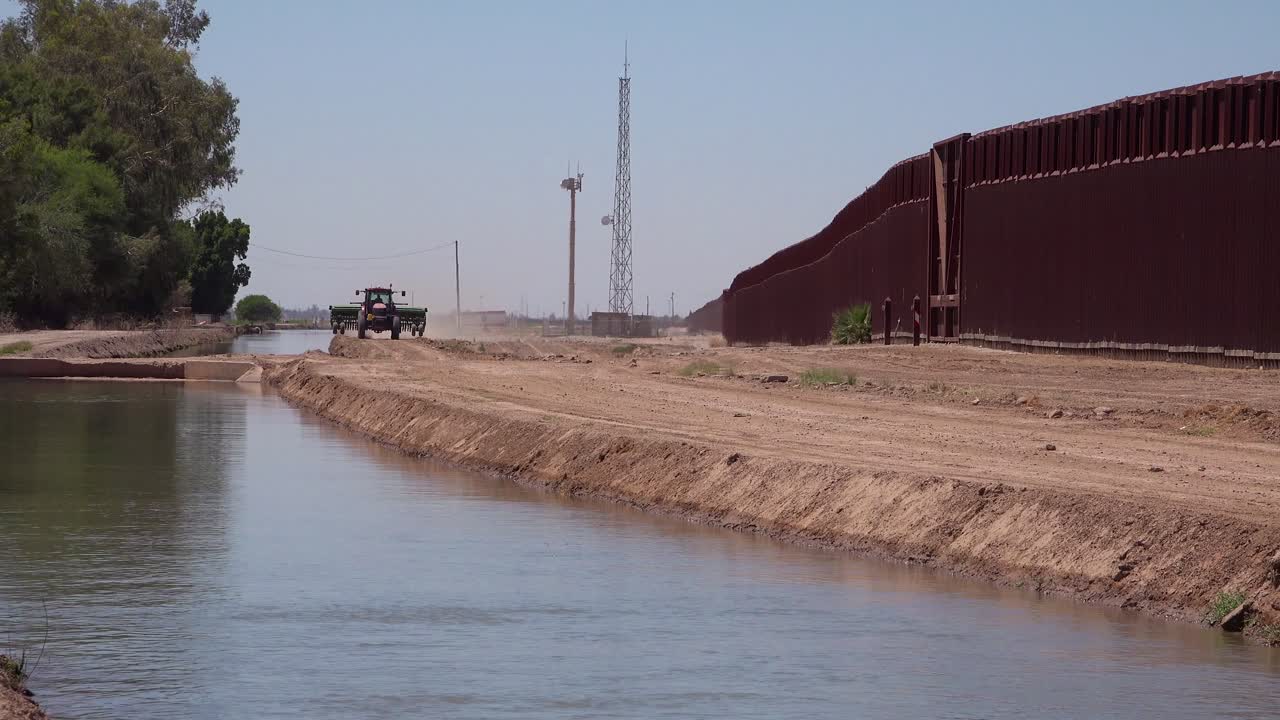 un tractor de agricultores sigue un afluente del río colorado a medida que fluye a lo largo del muro fronterizo entre los estados unidos y méxico