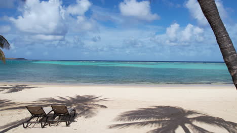 Idyllic-Holiday-Destination-Scenery,-Sunbeds-Under-Palm-Trees-on-White-Sand-Beach-and-Caribbean-Sea,-Drone-Shot