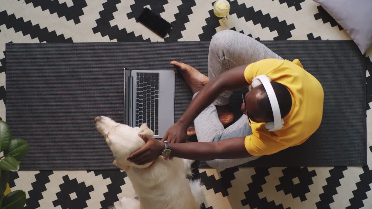 Afro-American Man Sitting on Floor with Laptop and Petting Dog