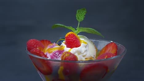 una tazza con palline di gelato, bacche, panna e salsa è guarnita con menta