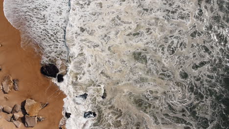 Sea-waves-crash-against-the-rocky-shoreline-in-Nazare,-Portugal,-a-destination-where-the-might-of-the-ocean-converges-with-the-diverse-expanse-of-rocky-shores