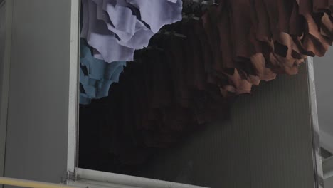 cueros de animales curtidos de color colgados en un estante automático industrial de secado de cuero en una planta textil
