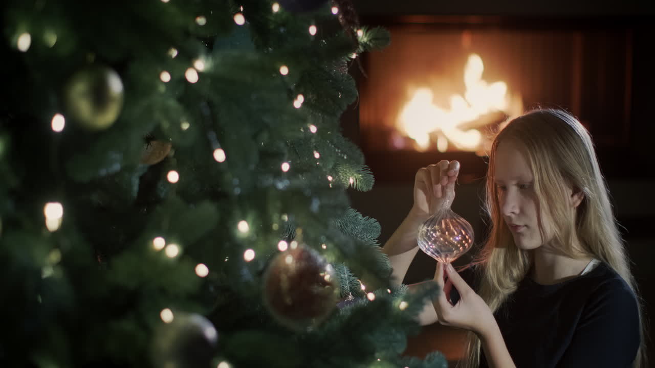 The girl is sitting near a beautiful Christmas tree, holding a toy in her hands. Preparing to celebrate Christmas
