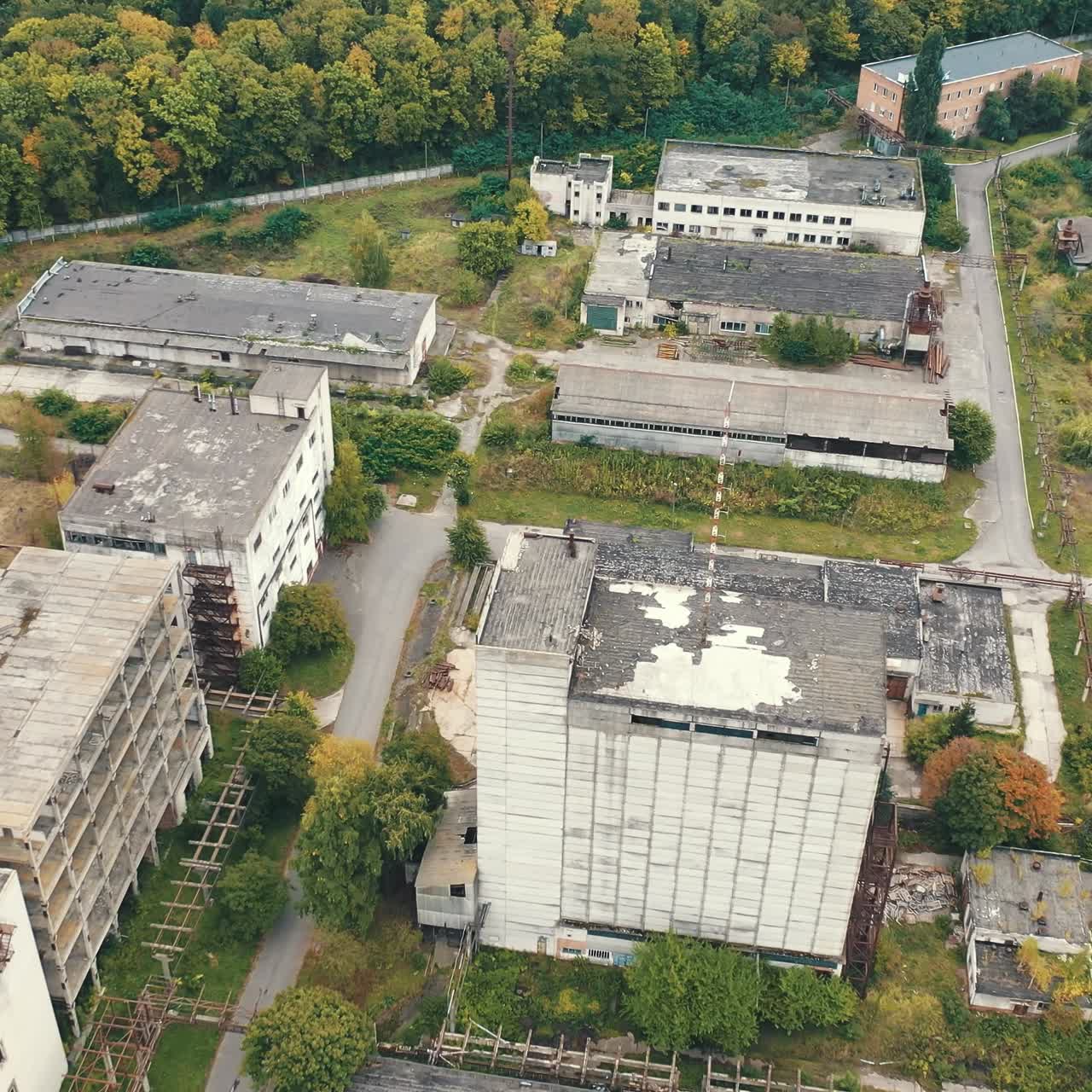 Empty factory constructions. Flight over abandoned buildings with old roofs. Ruined industrial territory near the forest