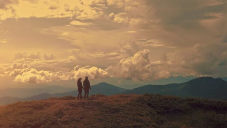 the man and woman standing on the  mountain top against the sunset