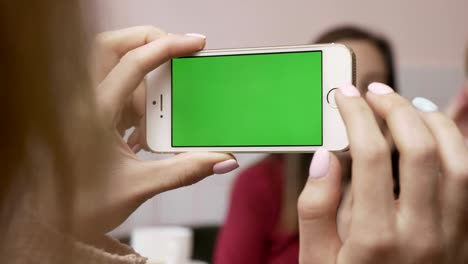 joven hermosa chica caucásica está haciendo una foto en el teléfono inteligente de sus dos amigas sentadas en un café. amigas en el concepto de café. usando un teléfono inteligente chromakey, pantalla verde. cerrar 60 fps