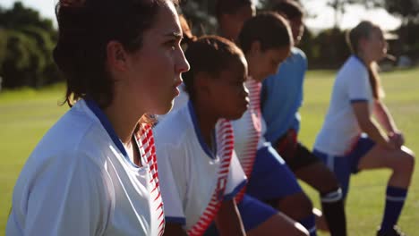 Female-soccer-players-stretching-their-legs-on-soccer-field.-4k