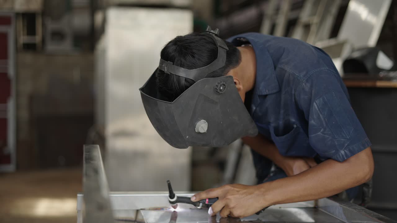 A person welding metal with a welding mask in a workshop