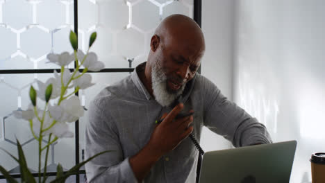 man talking on landline while using laptop on desk 4k