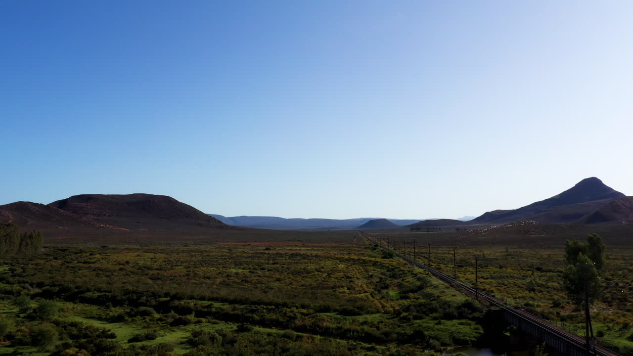 외딴 풍경에 있는 두 산맥 사이의 빈 철로를 따라 무성한 녹색 풍경의 공중 드론 샷