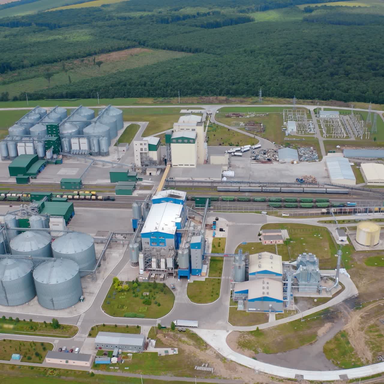 Industrial factory with grain elevators in field. Agriculture harvest storage on the background of beautiful nature landscape. Aerial view