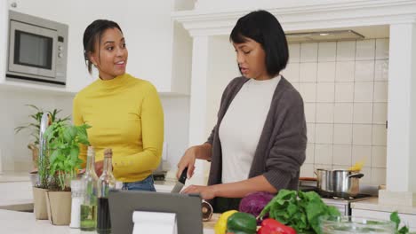 Happy-biracial-sisters-cooking-dinner-together-in-kitchen,-in-slow-motion