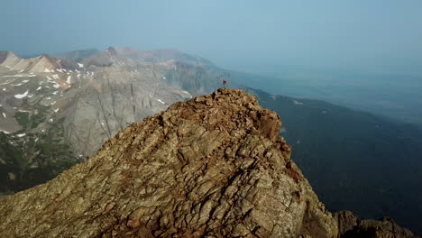 vista aérea de la persona en la cima de la cumbre de la montaña rocosa con una vista impresionante del rango en un día soleado, revelando un disparo de drones