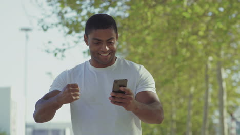 Smiling-young-muscular-man-using-smartphone-during-stroll.