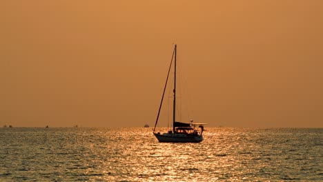 Hermosa-Silueta-De-Un-Yate-Con-Una-Puesta-De-Sol-Naranja-Brillante-En-El-Fondo-Con-Reflejos-En-Las-Aguas-Oceánicas-De-Bangsaray-Cerca-De-Pattaya,-Thaland