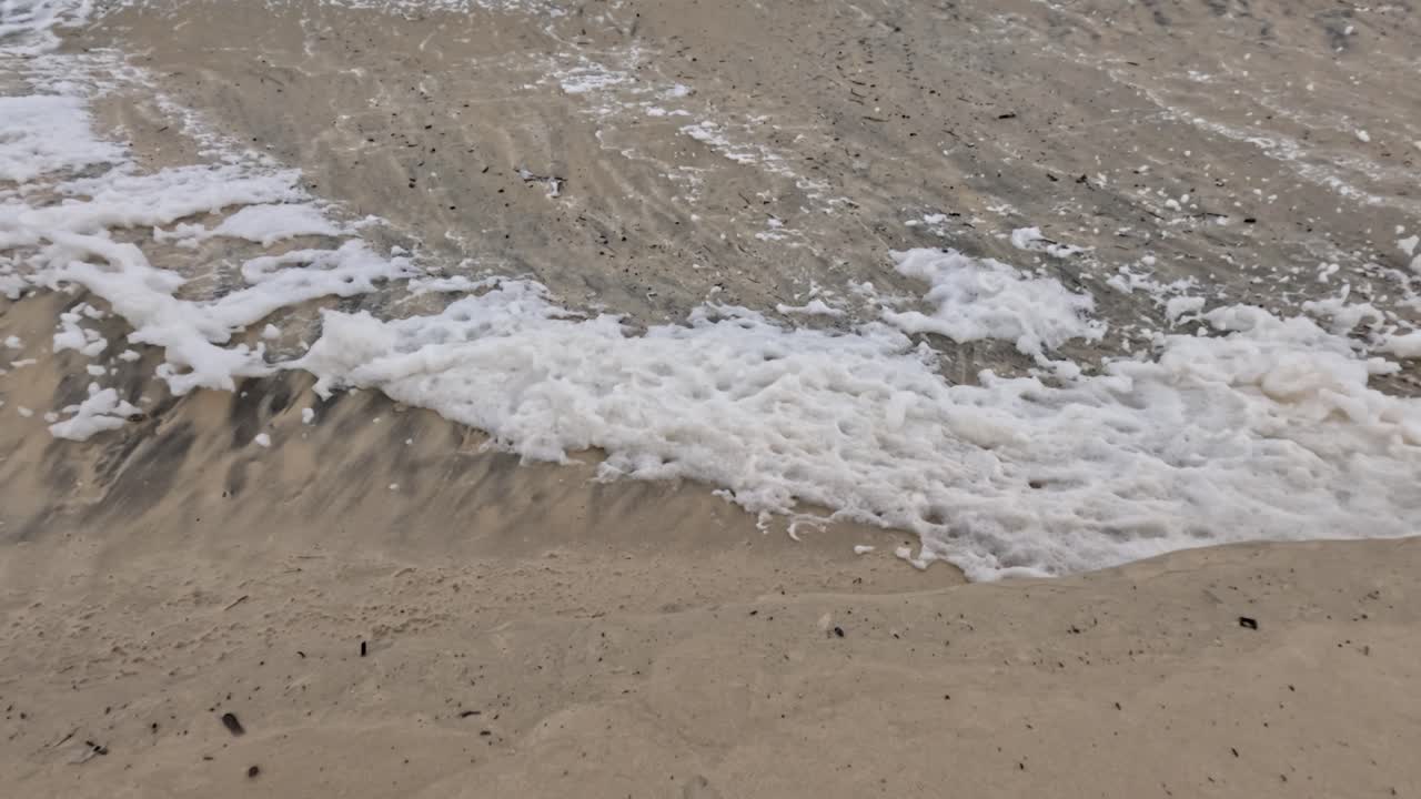 파도가 모래 해변에 부히면서 거품과 패턴을 만들어내며 물과 모래 사이의 역동적인 상호 작용을 포착합니다.