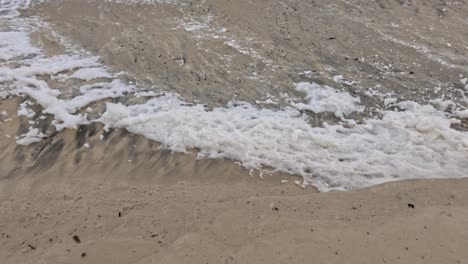 waves crash onto a sandy beach, creating foam and patterns. the scene captures the dynamic interaction between water and sand