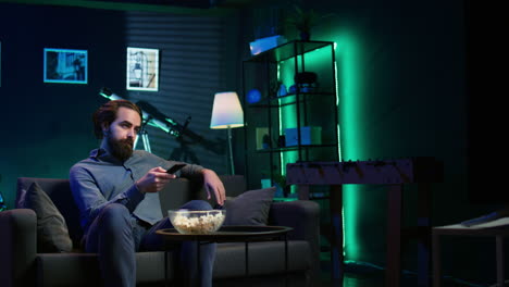 man on couch browsing though movies on streaming service using remote control