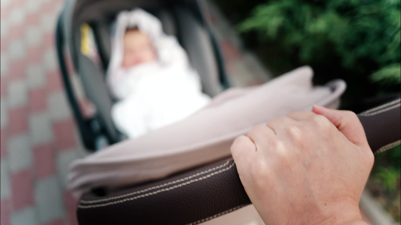 Close up of a parent's hand pushing a stroller handle while walking in a park