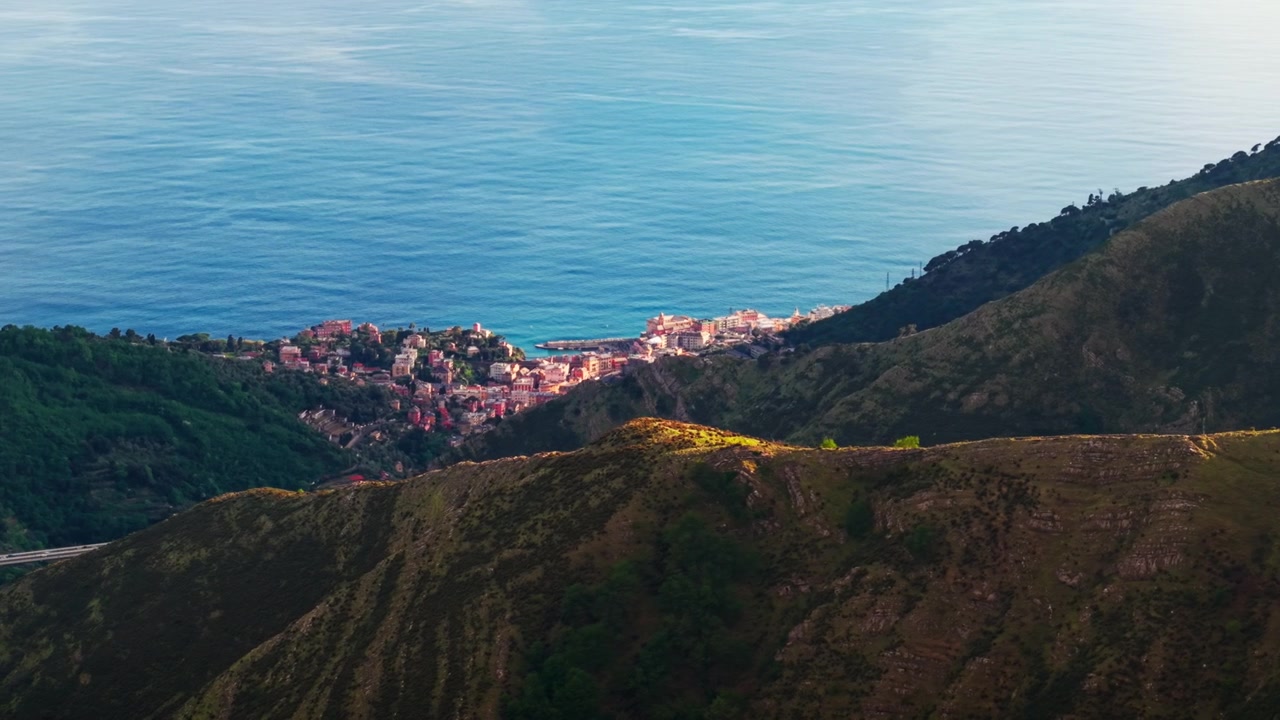 Una splendida prospettiva aerea con drone di un iconico edificio rosso annidato sulla costa rocciosa tra il mare blu e le aspre scogliere montuose della Liguria, Italia.