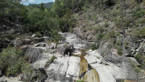 Drone-flying-over-people-relaxing-on-rocks-of-Cascatas-de-Fecha-de-Barjas-in-Peneda-Geres-National-park,-Portugal