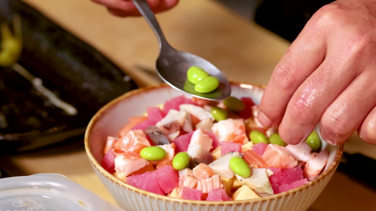 Primo piano delle mani che preparano una poke bowl salutare con pesce crudo ed edamame.