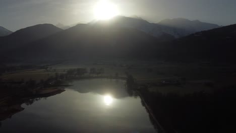 Aerial-over-a-lake-early-in-the-morning,-with-the-reflection-of-the-sun-rising-over-mountains