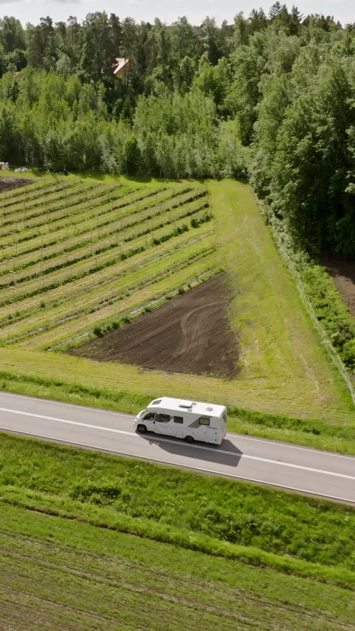 Vertical drone shot following a camper van driving in middle of rural plantations