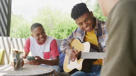 Happy-diverse-male-teenage-friends-playing-guitar-at-home,-slow-motion