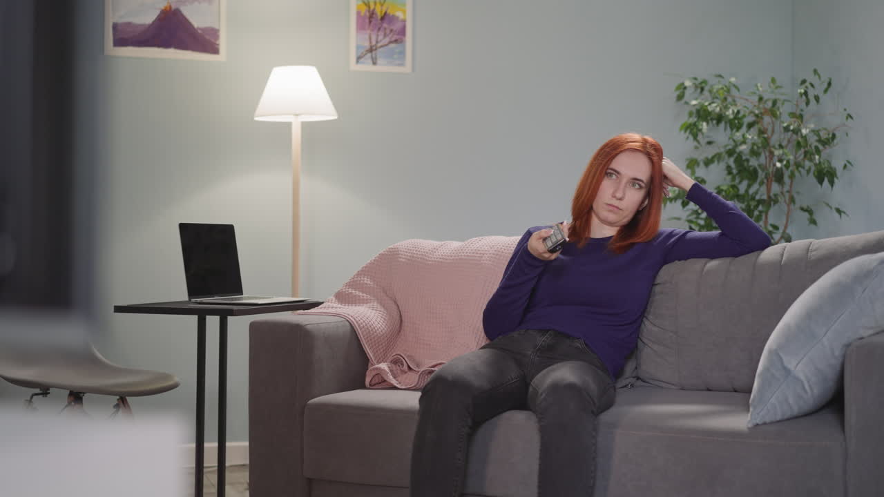 과로 한 주부 는 tv 에서 채널 을 바꾸는 소파 에 앉아 있다