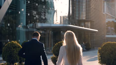 rear view of two business people walking to office entrance at sunrise - slow motion. man and woman coworkers going to corporate building in the morning with sun rising in background