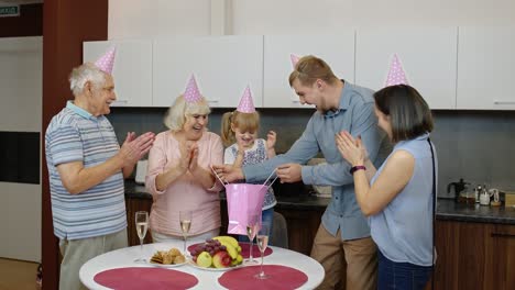 Mother,-father-and-grandparents-giving-gift-bag-for-child-girl.-Celebrating-birthday-anniversary