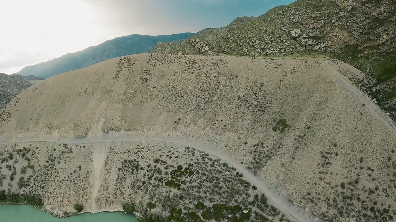 пустая дорога на горном склоне над рекой fpv дрон. тропа привлекательна для путешественников для живописной привлекательности, предлагающей захватывающие виды. путь на крутом склоне