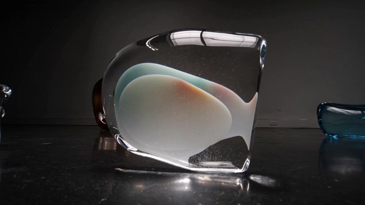Tilting glass paperweight rotating on display, showing white core, teal inclusion, orange accent