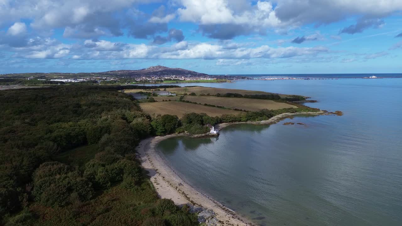 Aerial view rising over Welsh crescent bay under idyllic Holyhead mountain and distant farmland
