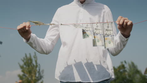un hombre sostiene un cordón de la ropa en sus manos, en el que cuelgan billetes de banco. concepto de lavado de dinero. toma de bajo ángulo