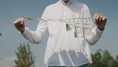 a man holds a clothesline in his hands, on which banknotes hang. money laundering concept. low angle shot