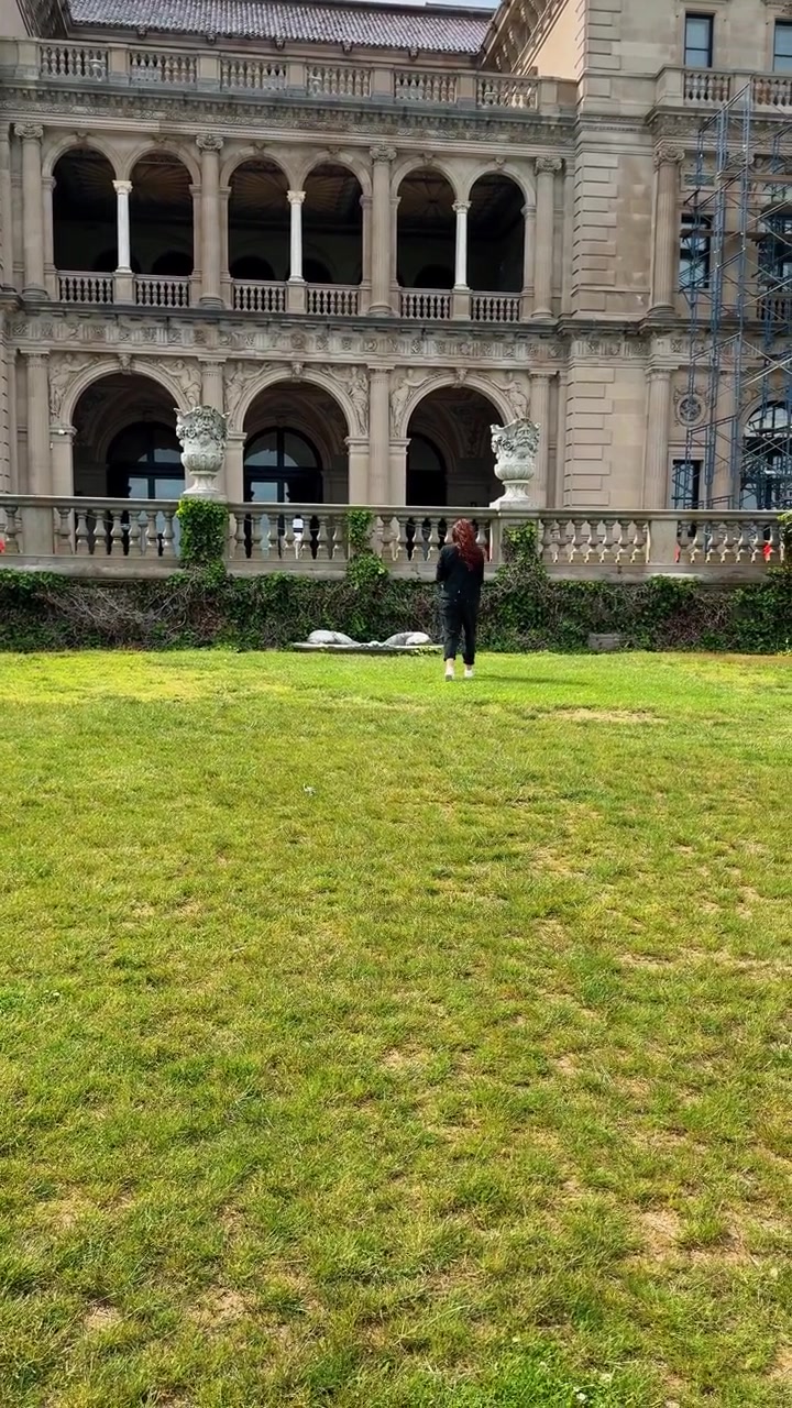 Boston, USA, 5 maggio 2025: Vista posteriore di una donna che si avvicina a un grande palazzo in pietra. Donna con capelli lunghi che cammina sull'erba verde verso l'imponente facciata di una lussuosa tenuta storica.