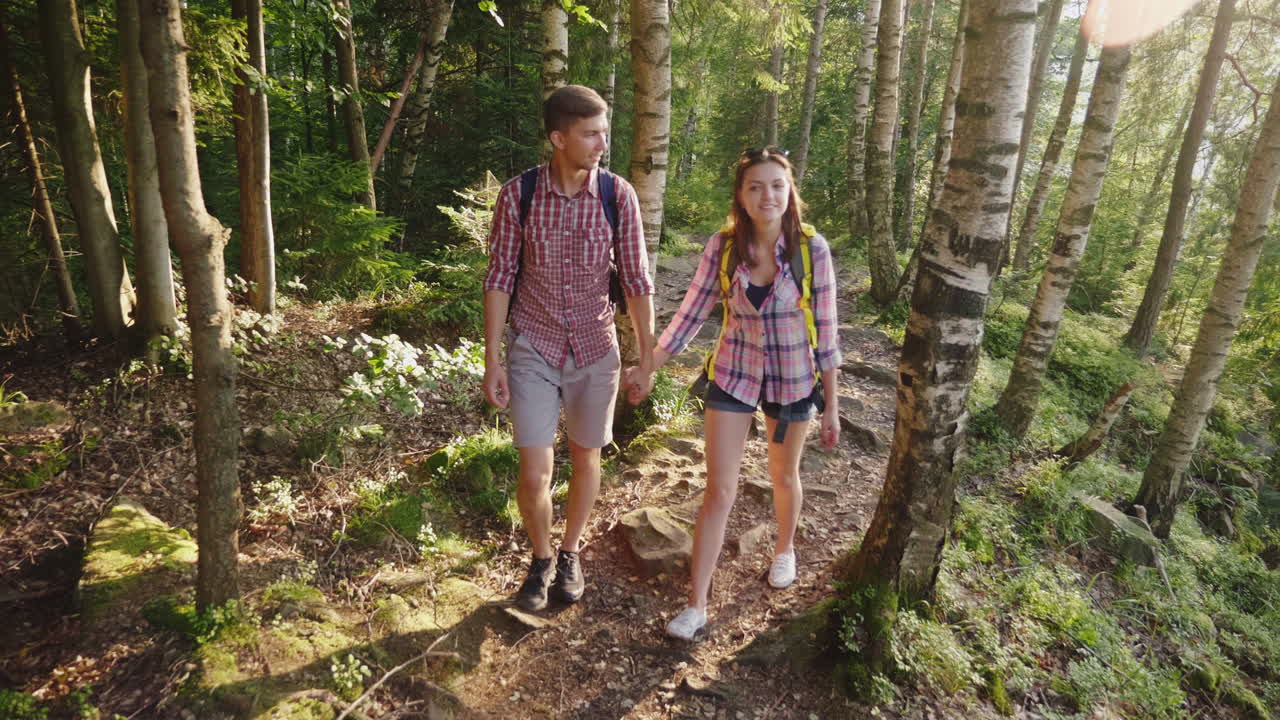 Una giovane coppia di turisti cammina lungo un sentiero di montagna sotto i raggi del sole che tramonta.