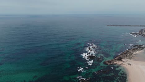 Aerial-view-of-serene-coastal-waters-with-rocky-shorelines-and-sandy-beach-at-Caxinas,-Portugal