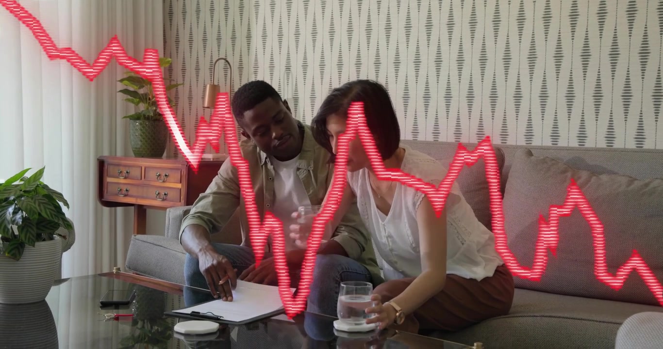 Man writing notes as red stock graph fluctuating causing woman bringing water studying stock data
